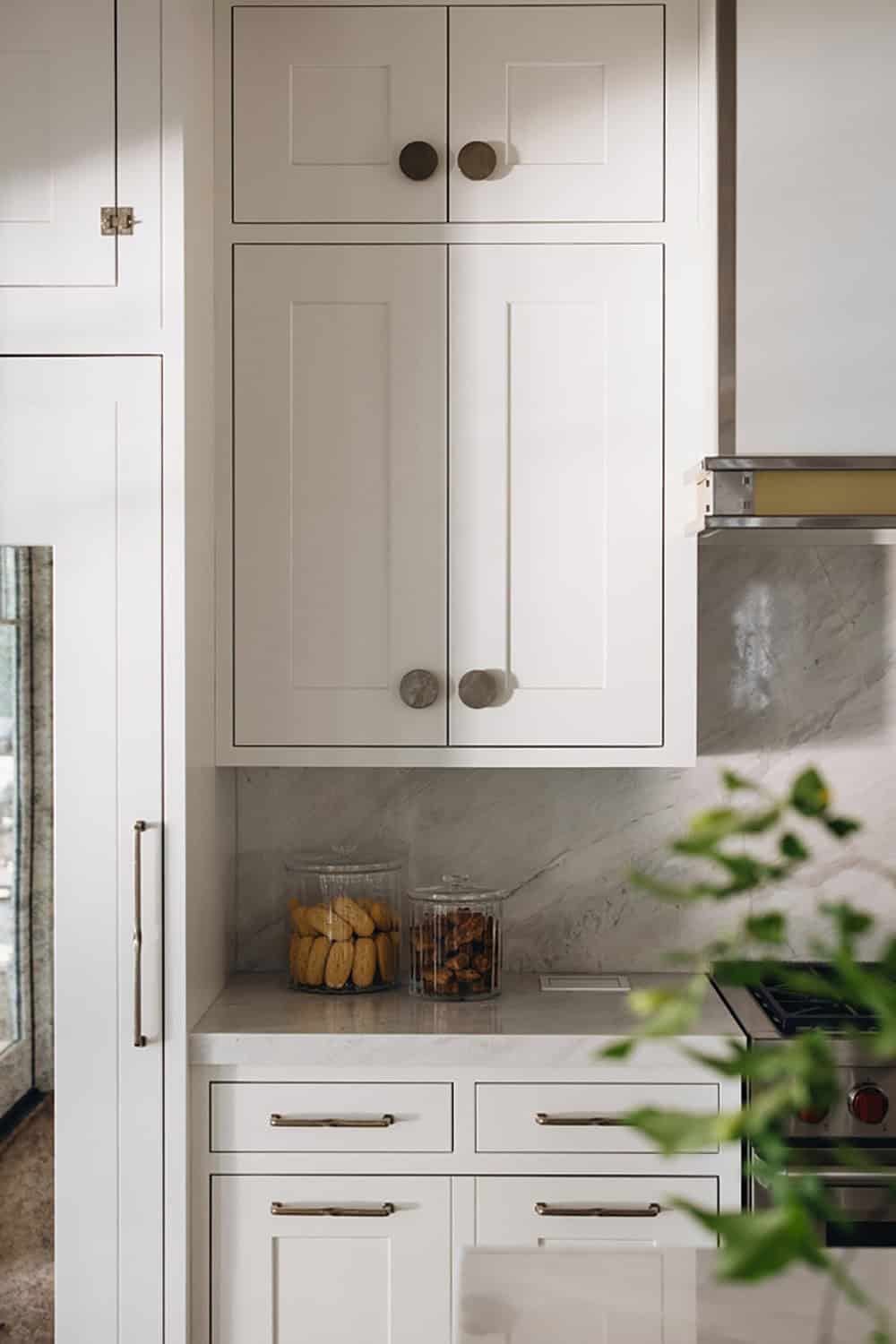 Close-up of white kitchen cabinetry with round hardware and marble backsplash