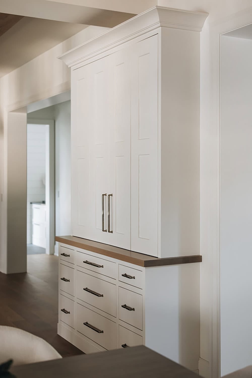 Tall white pantry cabinet with brass pulls beside a wood countertop