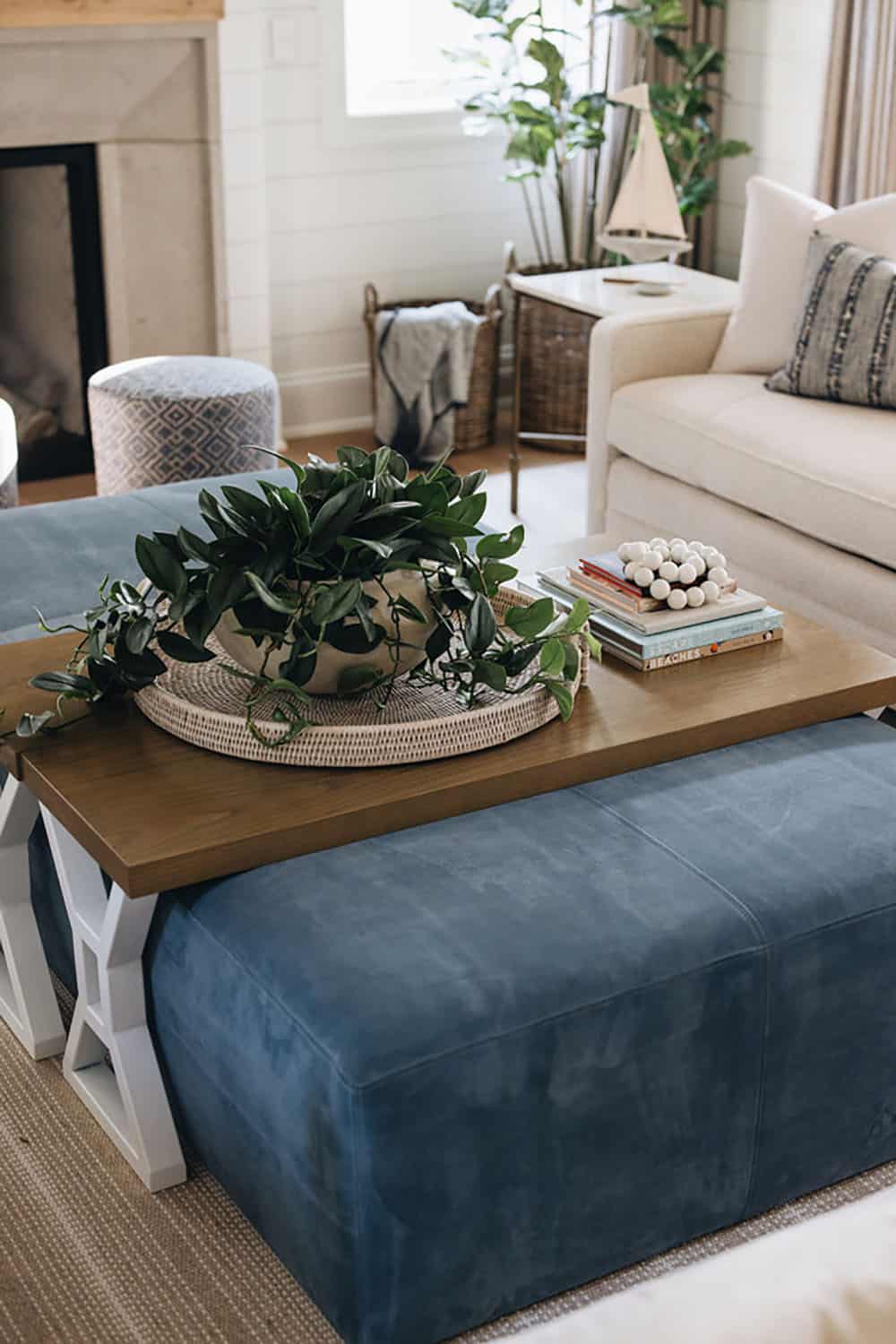 Coffee table styled with plant, tray, and stacked books beside blue ottoman