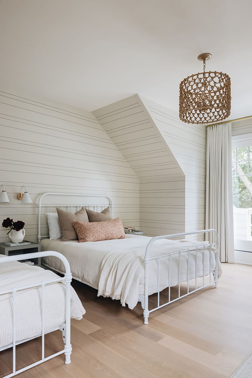 Kids' bedroom with two white iron beds and woven drum chandelier
