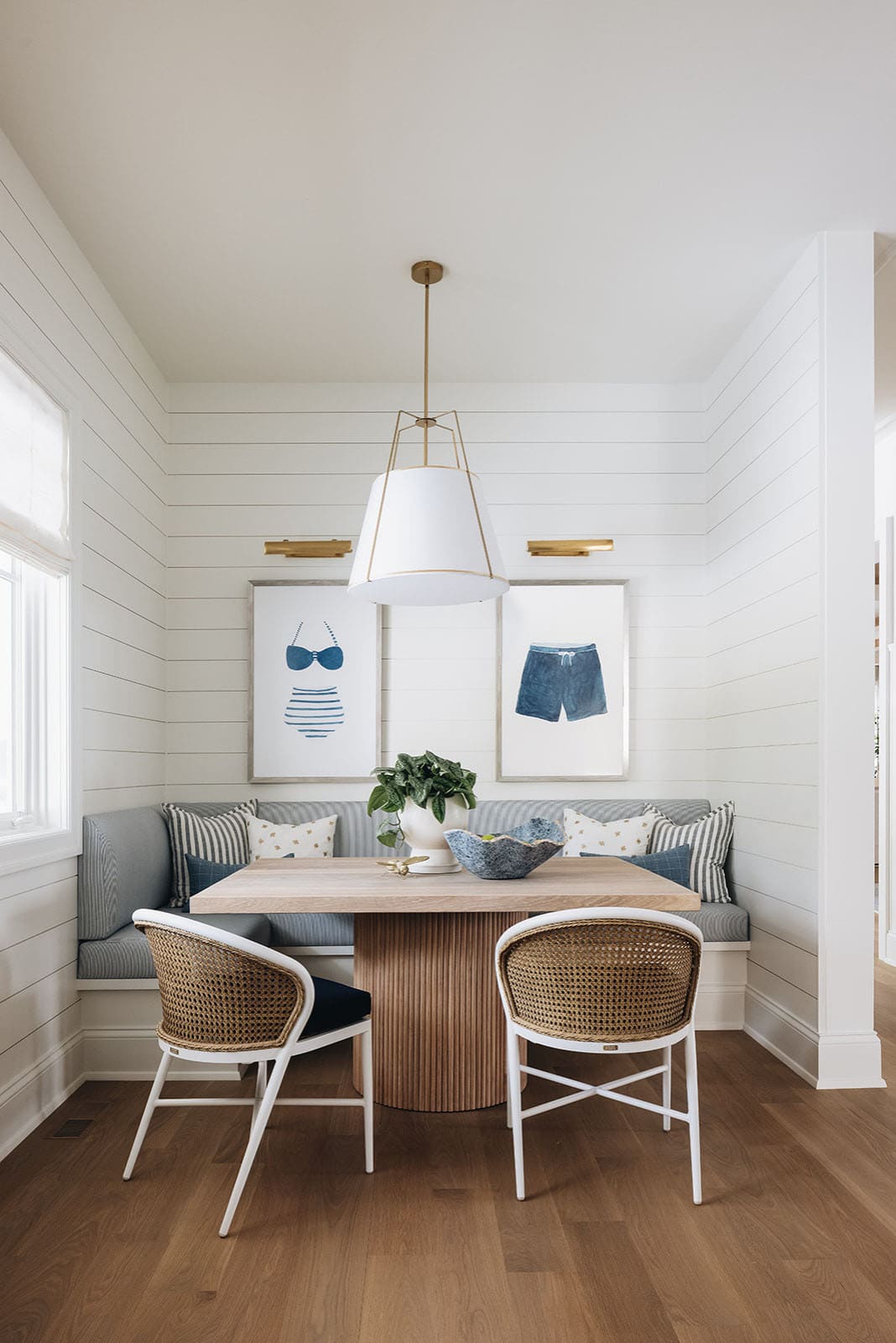 Breakfast nook with striped banquette, swimwear art, and woven chairs