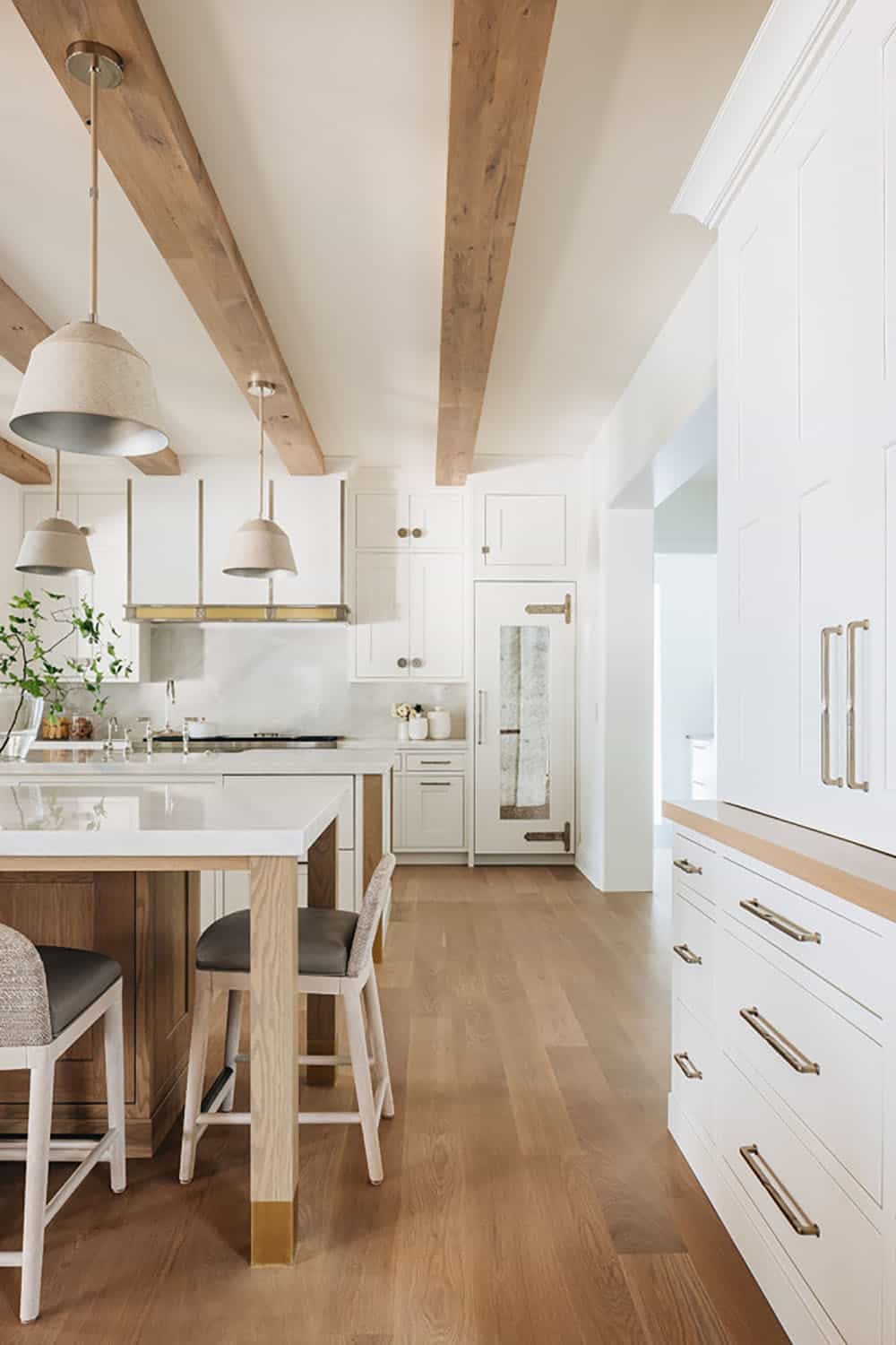 Kitchen hallway view with pendant lights, wood beams, and white cabinetry
