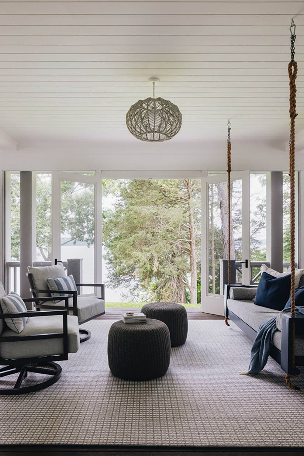 Screened porch with swing bed, woven ottomans, and lake view through trees