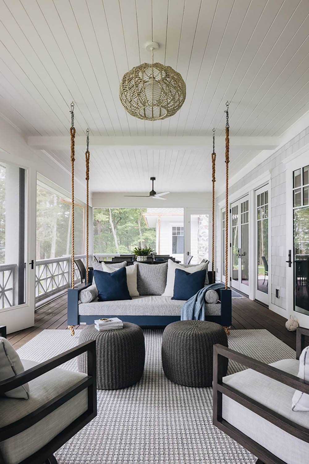 Screened porch with hanging bed swing, woven ottomans, and lounge chairs