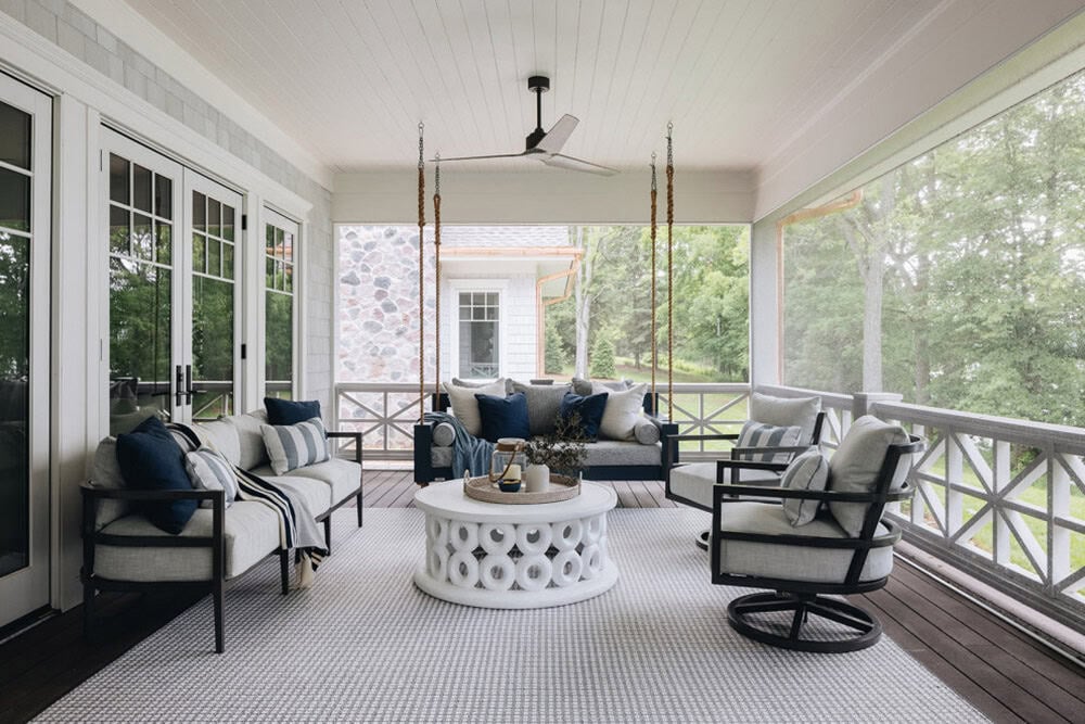 Screened porch seating area with swing bed, sofa, and round white coffee table