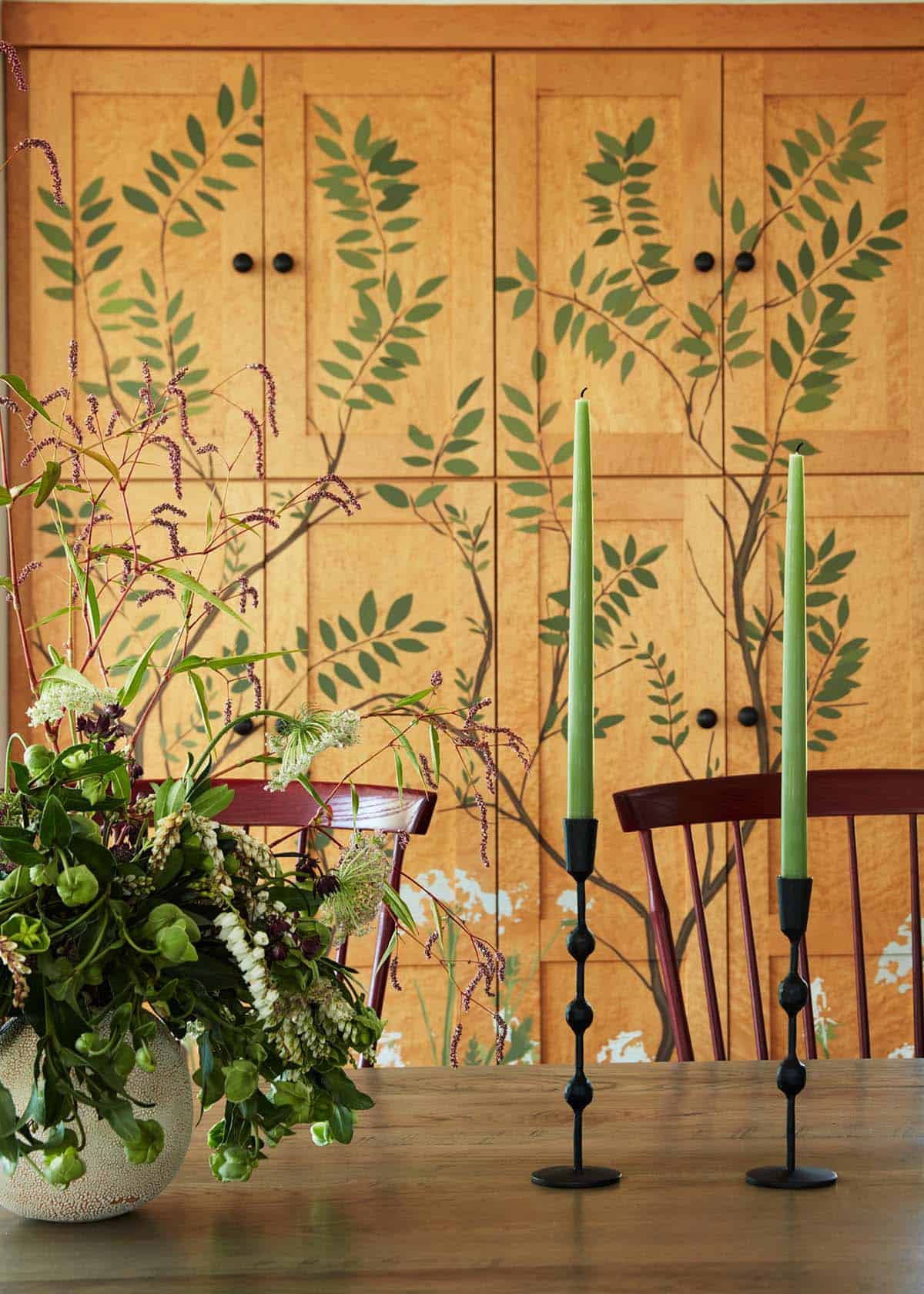 Hand-painted botanical cabinet detail with green taper candles