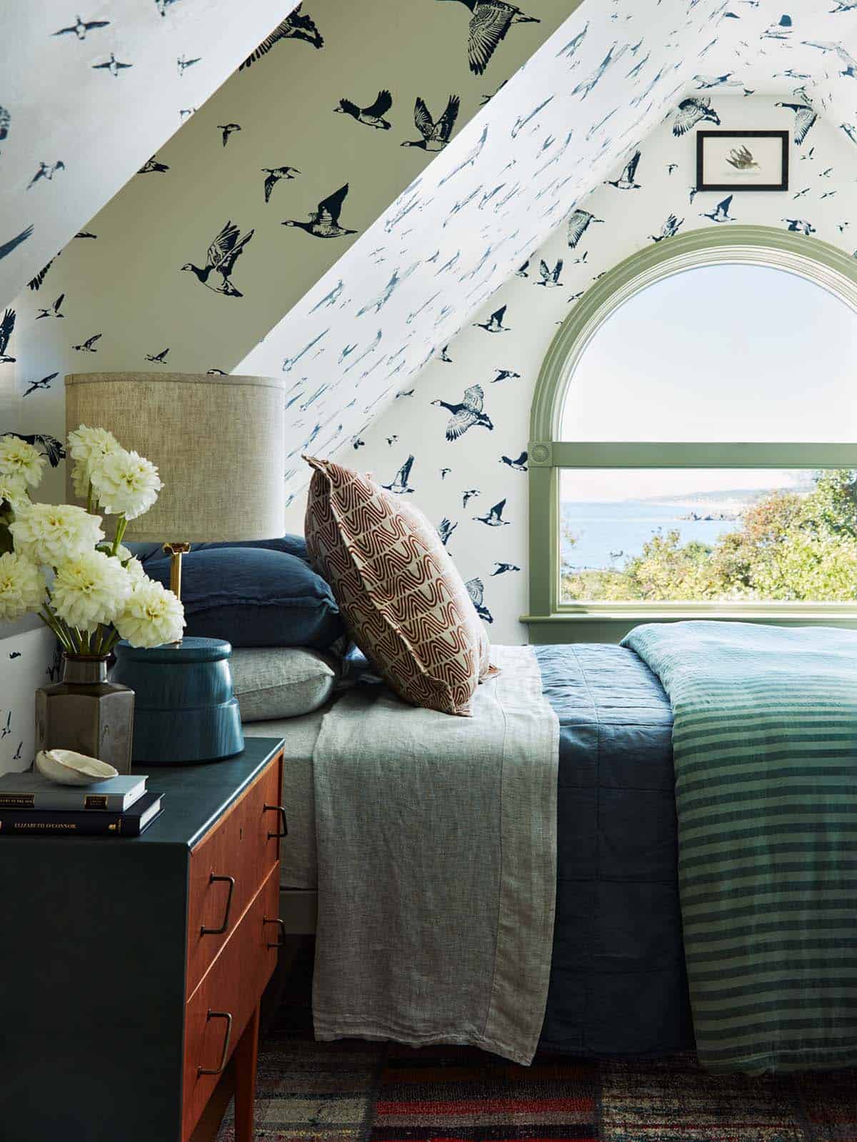 Guest bedroom with bird-print wallpaper and arched ocean-view window