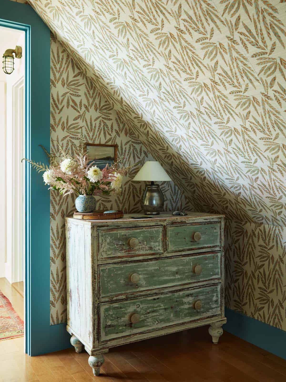 Distressed green dresser beneath leaf-print wallpaper
