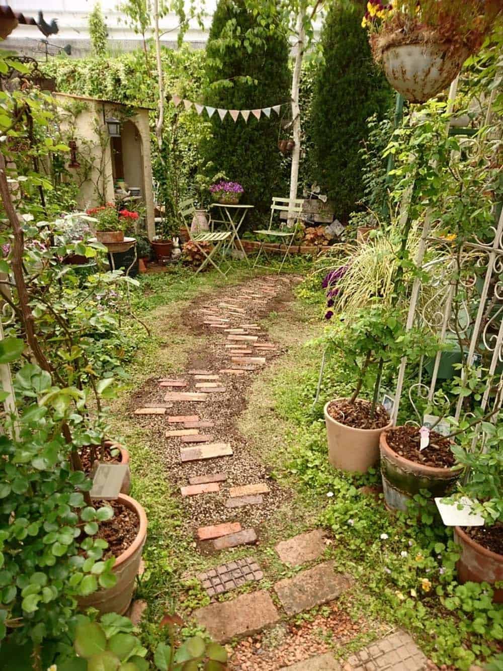 Reclaimed bricks laid flat and angled diagonally to form a staggered path through a lush potted-plant courtyard