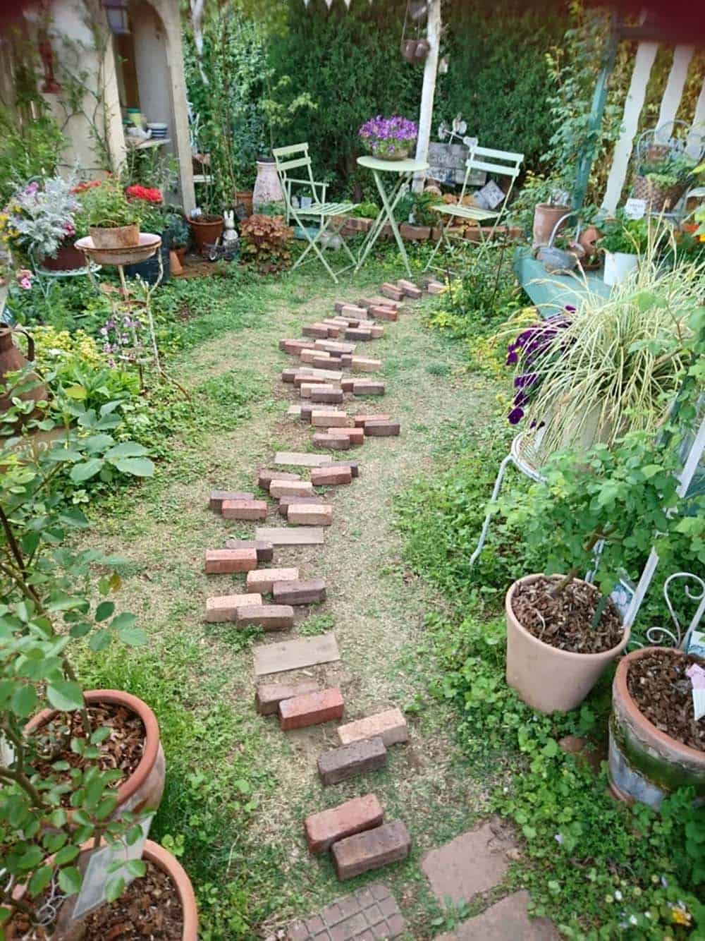 Loose bricks laid in pairs on grass to map out a garden path before installation, ahead of a small seating area