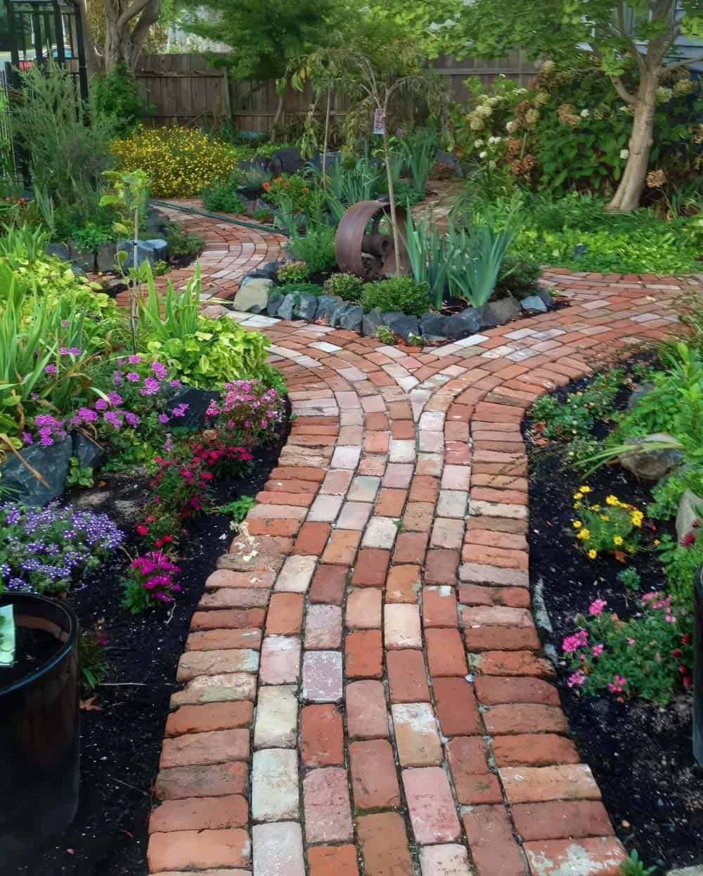 Wide reclaimed brick pathway laid in a running bond pattern that splits and curves around a central planted island bed