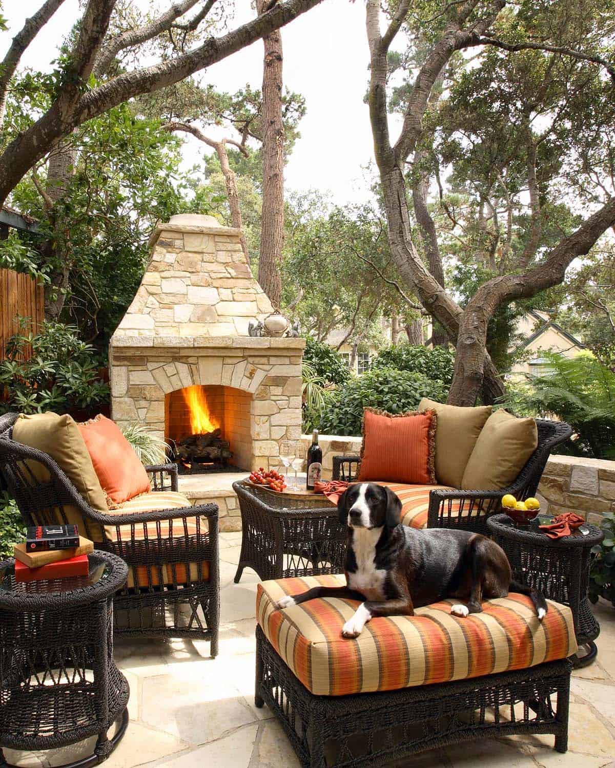 Tall stone fireplace with wicker seating on a tree-shaded patio
