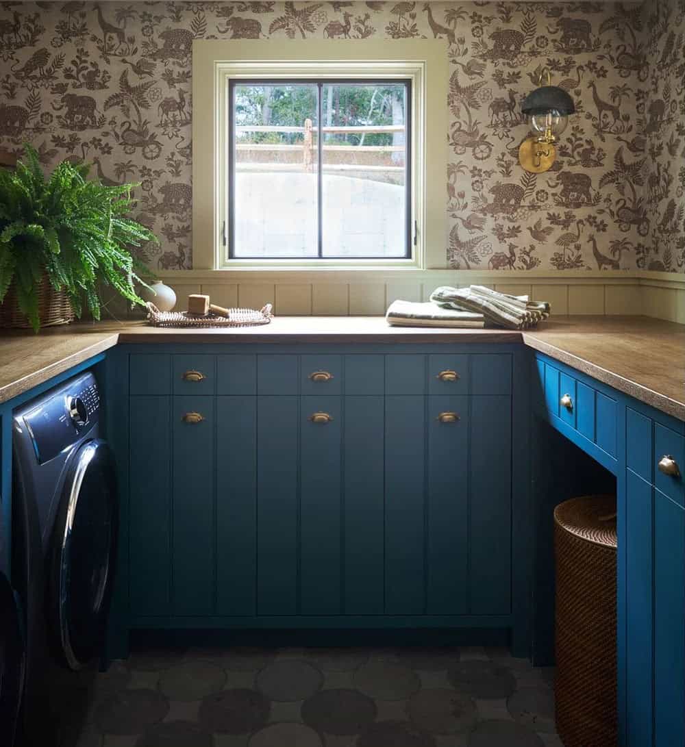 Teal laundry room cabinets with animal-print wallpaper and brass hardware