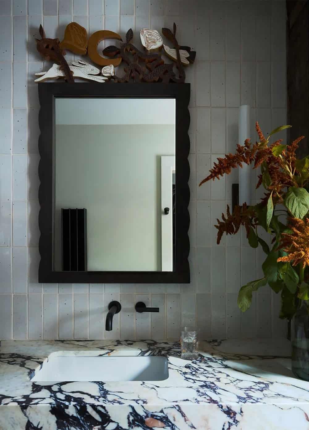 Bathroom mirror with carved wood topper above marble vanity