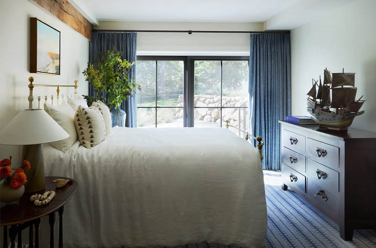 Bedroom with brass bed frame, blue drapes, and model ship dresser