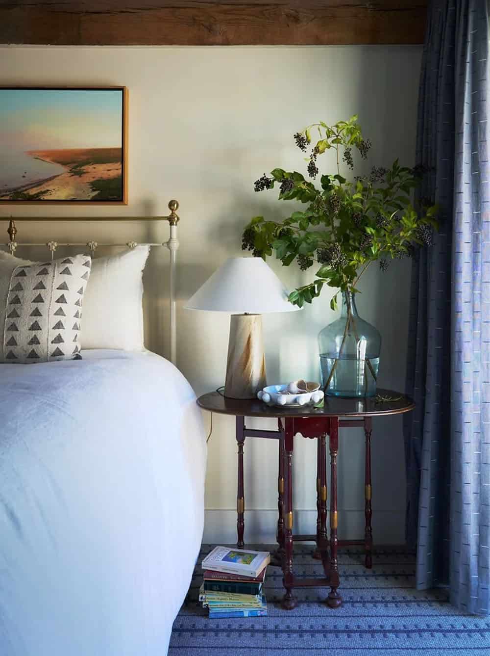 Bedside table with brass bed frame, glass vase, and coastal artwork