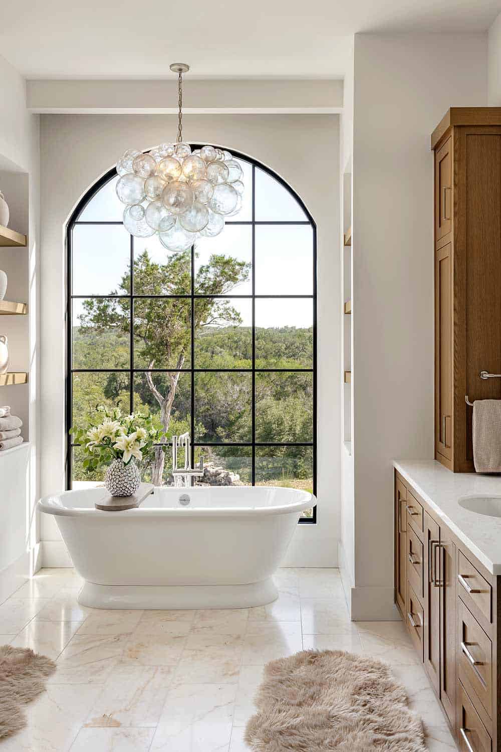 Freestanding tub beneath arched window and bubble glass chandelier