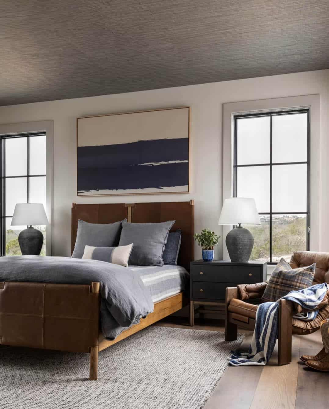 Guest bedroom with leather bed frame and navy landscape art