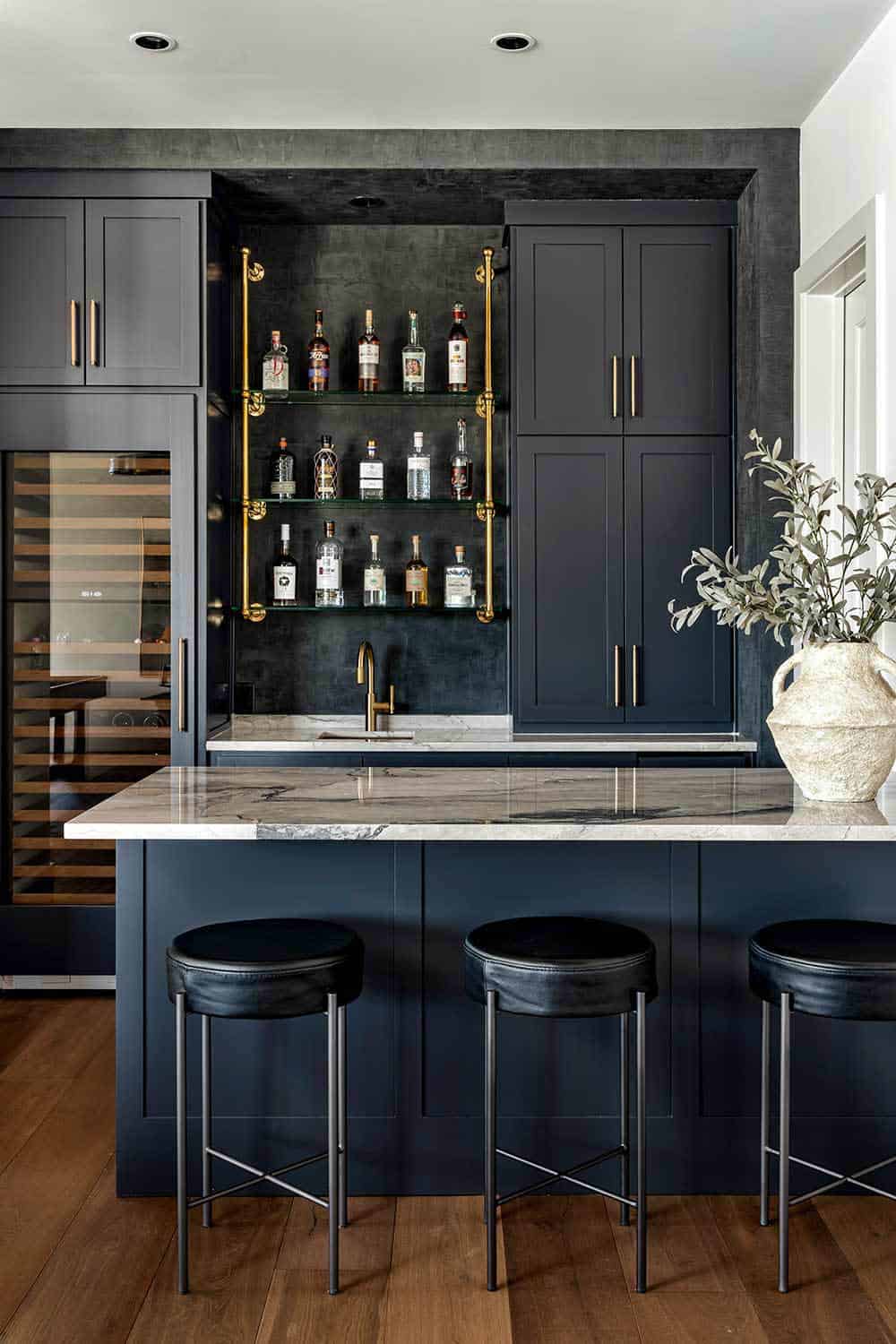 Wet bar with navy cabinetry and brass shelving for bottles