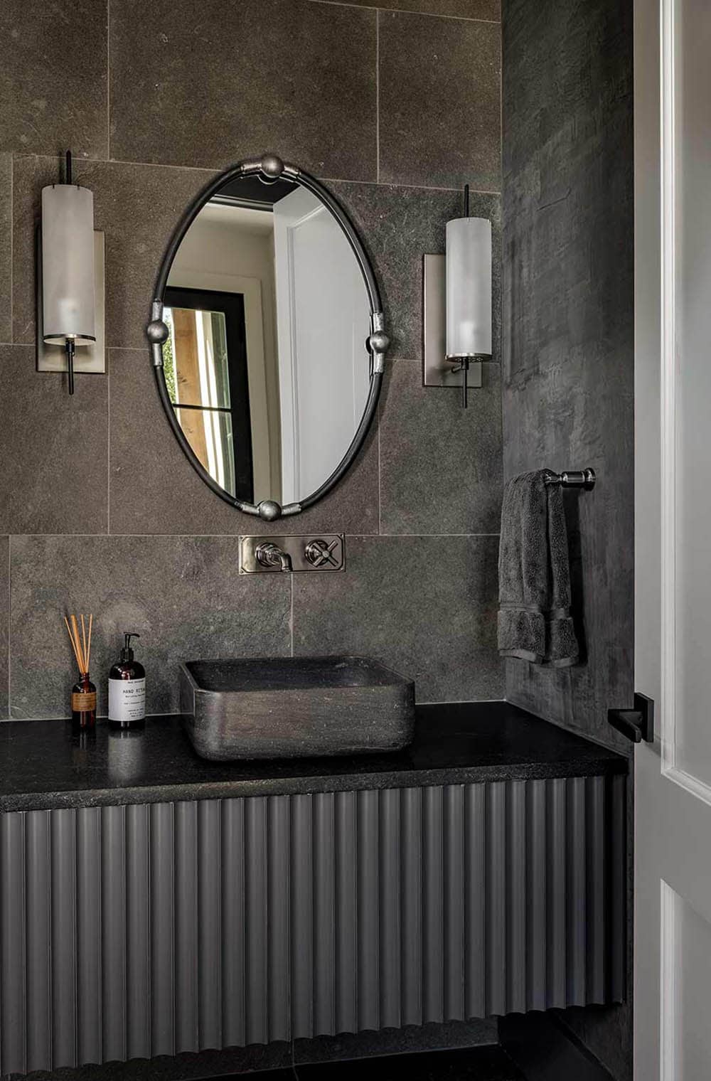 Powder room with oval mirror and stone tiled walls