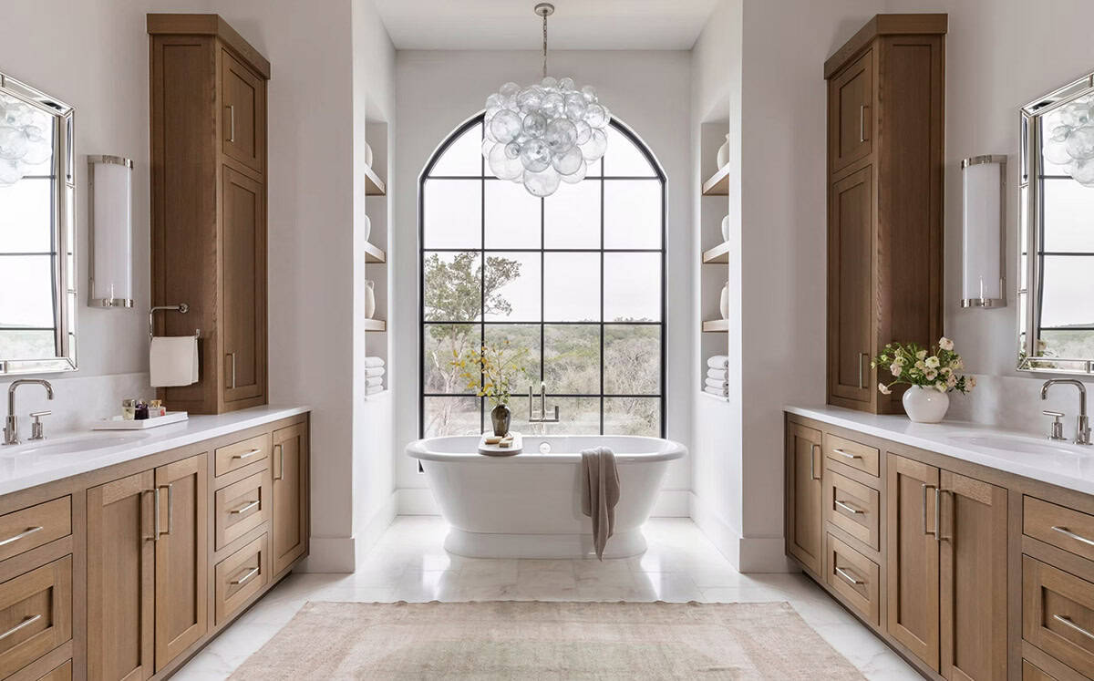 Primary bathroom with dual wood vanities and arched window tub nook