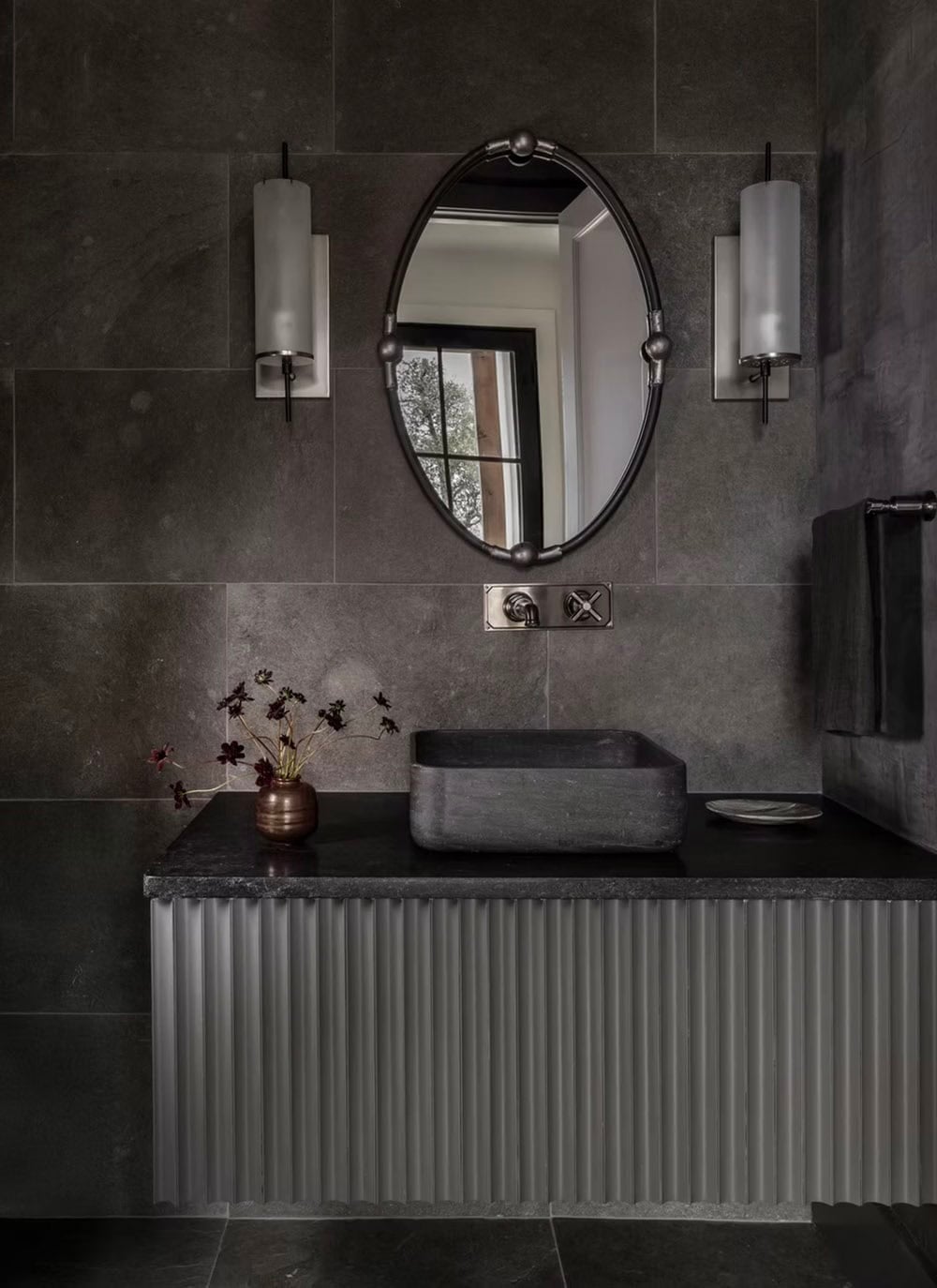Powder room with oval mirror and dark stone slab walls