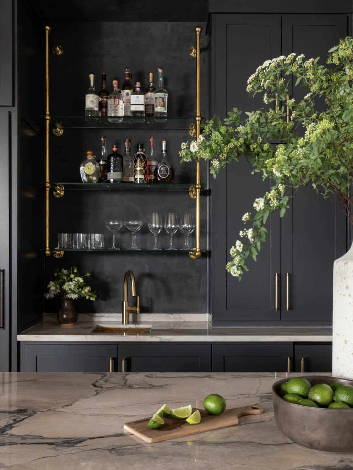 Wet bar with black cabinetry and brass shelving for glassware