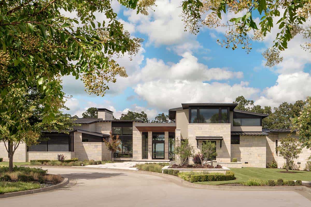 Stone and dark metal facade with covered entry beneath flowering trees