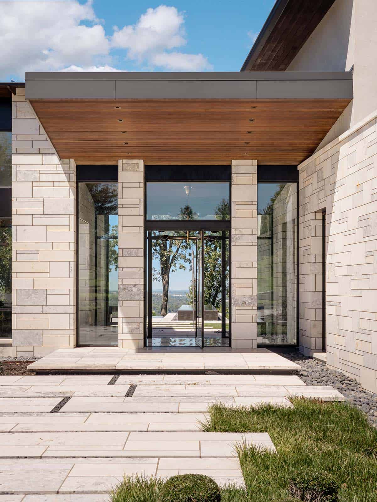 Wood-clad entry canopy above a glass pivot door and stone pathway