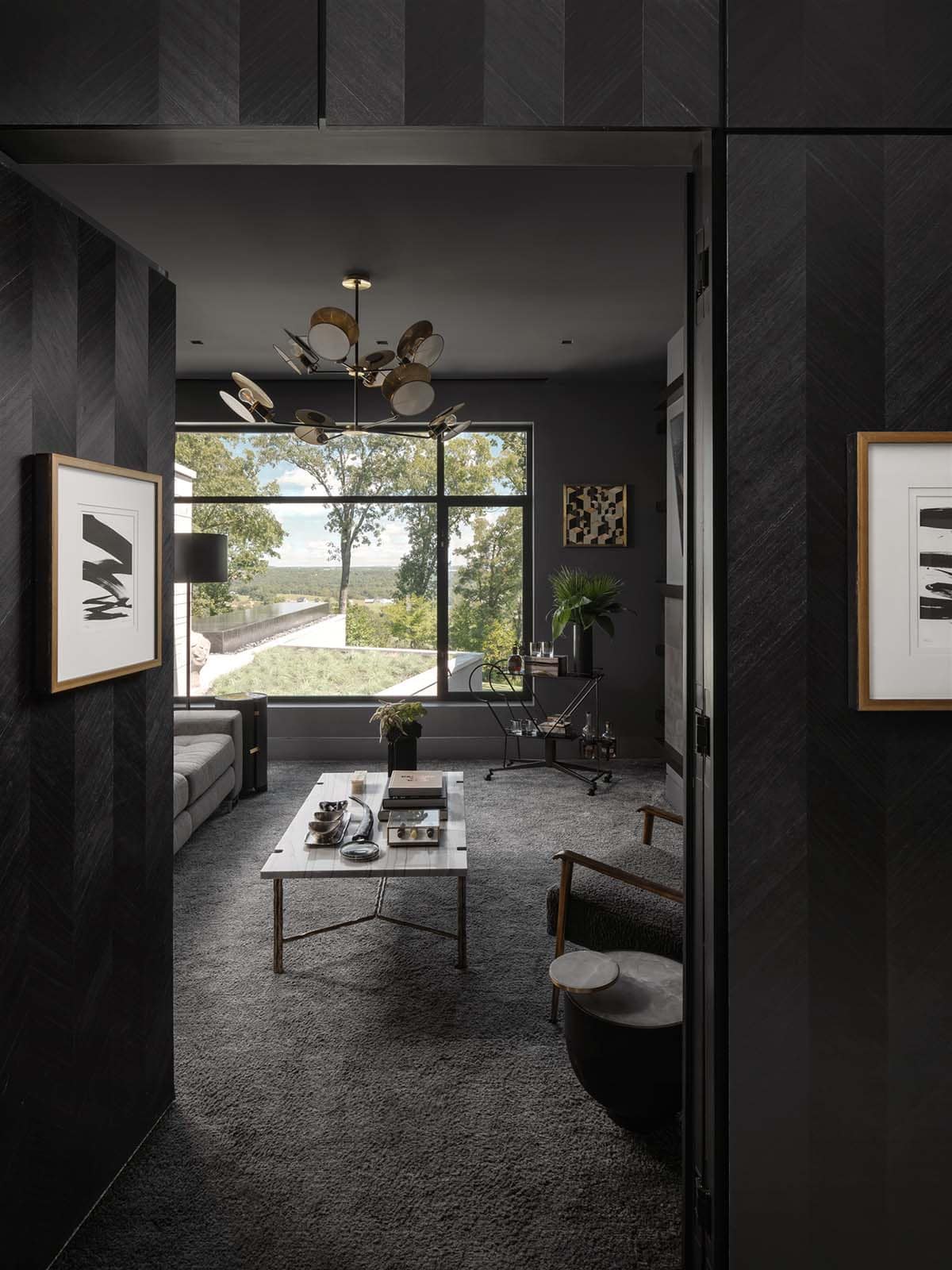 Charcoal lounge with brass chandelier and floor-to-ceiling forest views