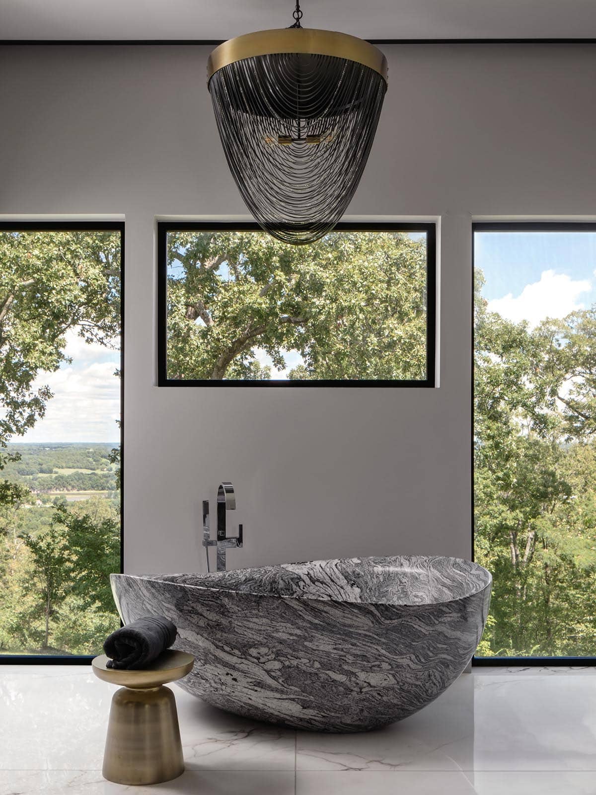 Sculptural stone soaking tub beneath a beaded brass pendant light