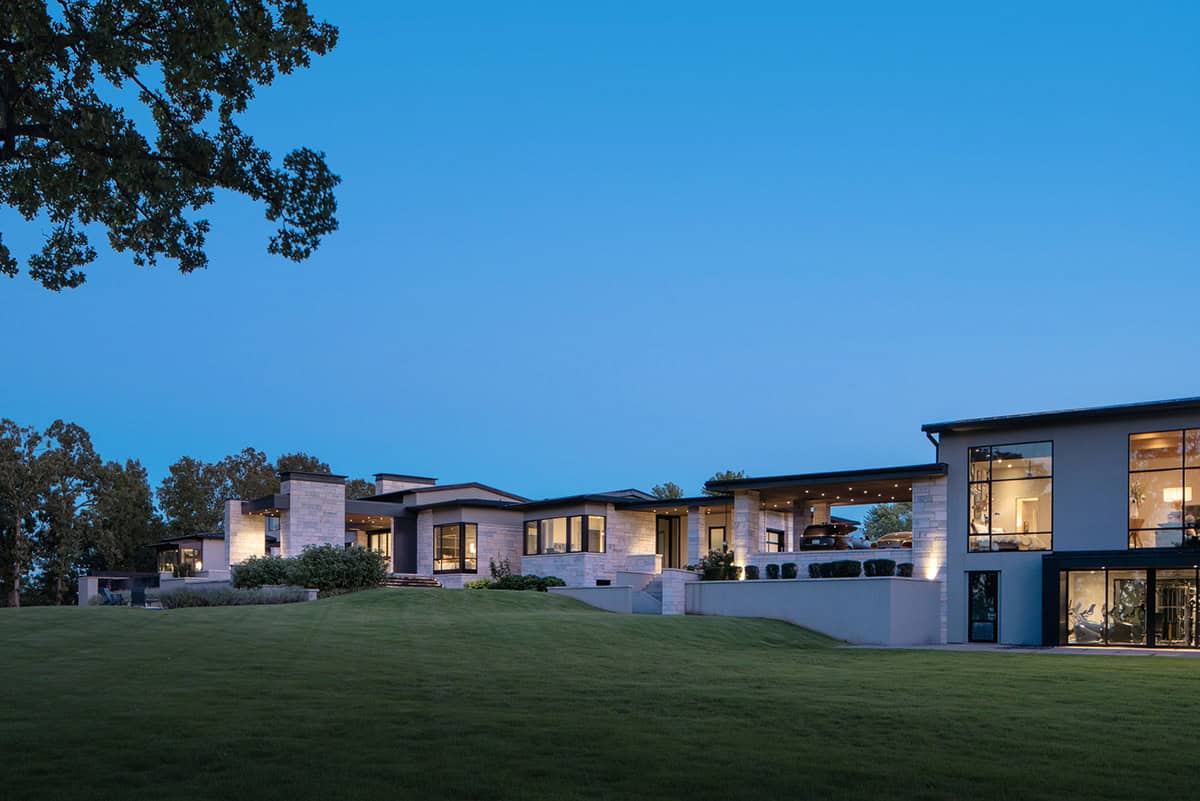 Dusk exterior showing illuminated stone home with covered motor court