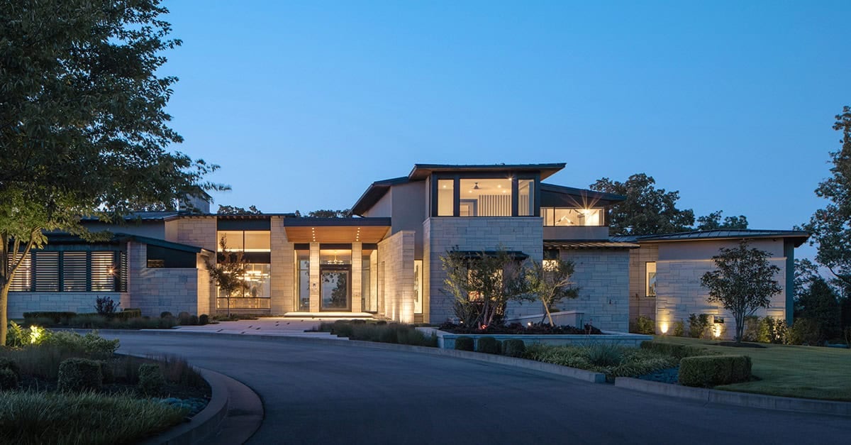 Front exterior with lit entry and curved driveway at dusk