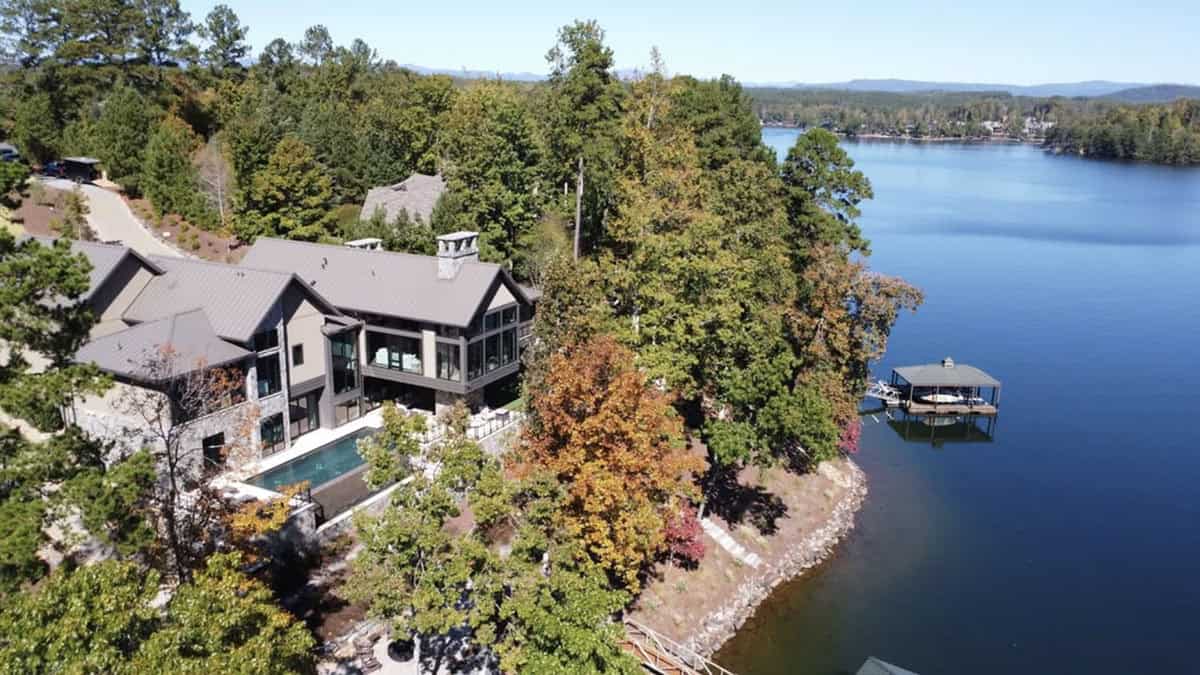 Aerial view of a contemporary lake house on a wooded shoreline with infinity pool and private dock