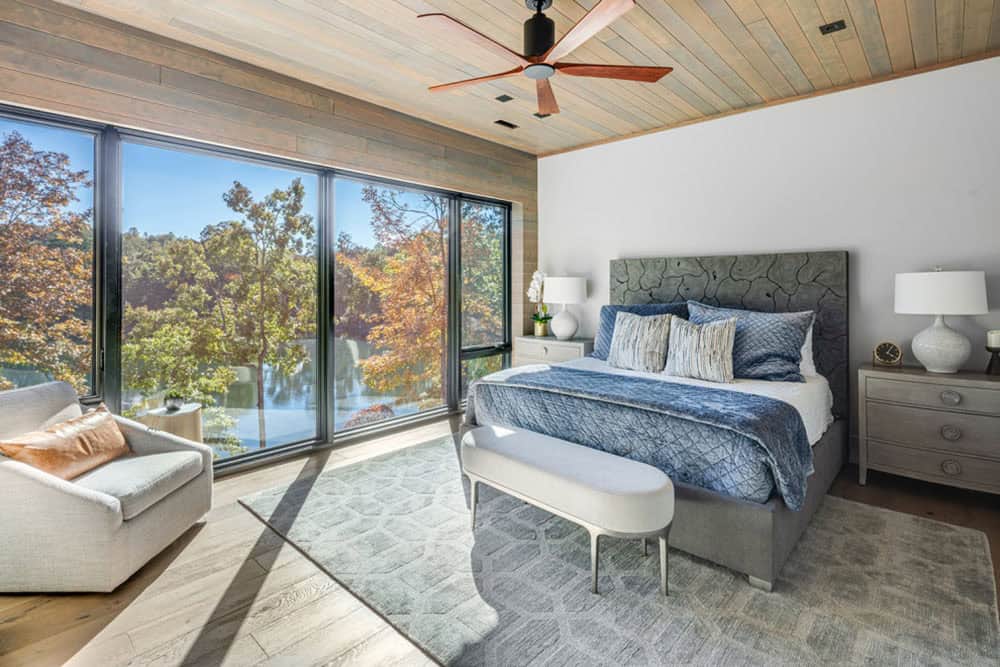 Primary bedroom with wood-plank ceiling, lake-view windows, and gray upholstered bed