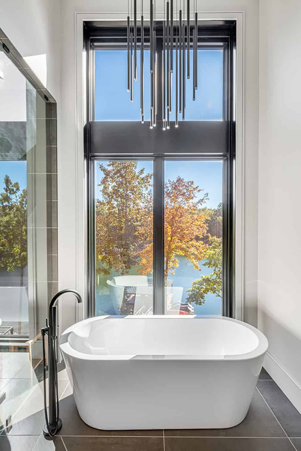 Freestanding white soaking tub beneath a tall window with a linear pendant light fixture