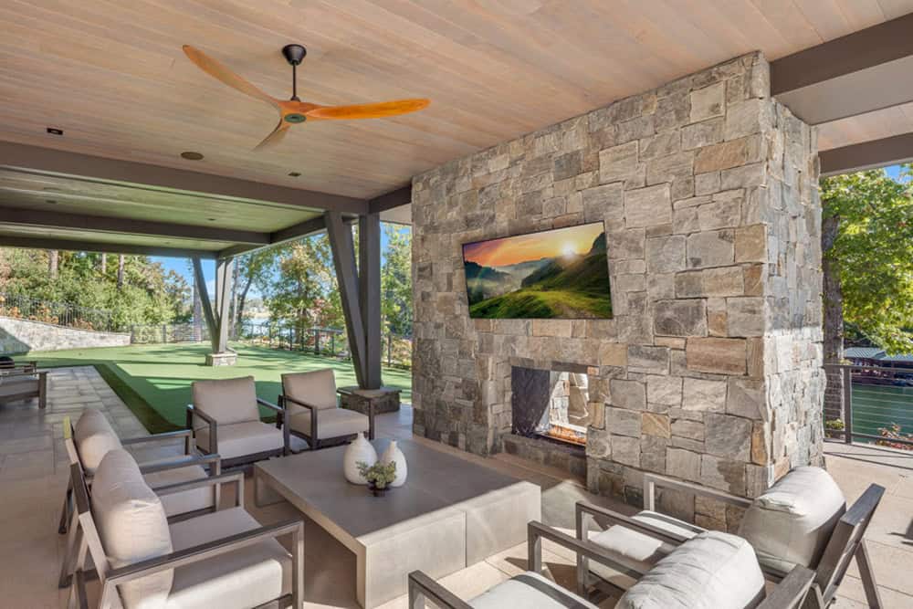 Covered outdoor living area with stone fireplace, TV, and lounge seating
