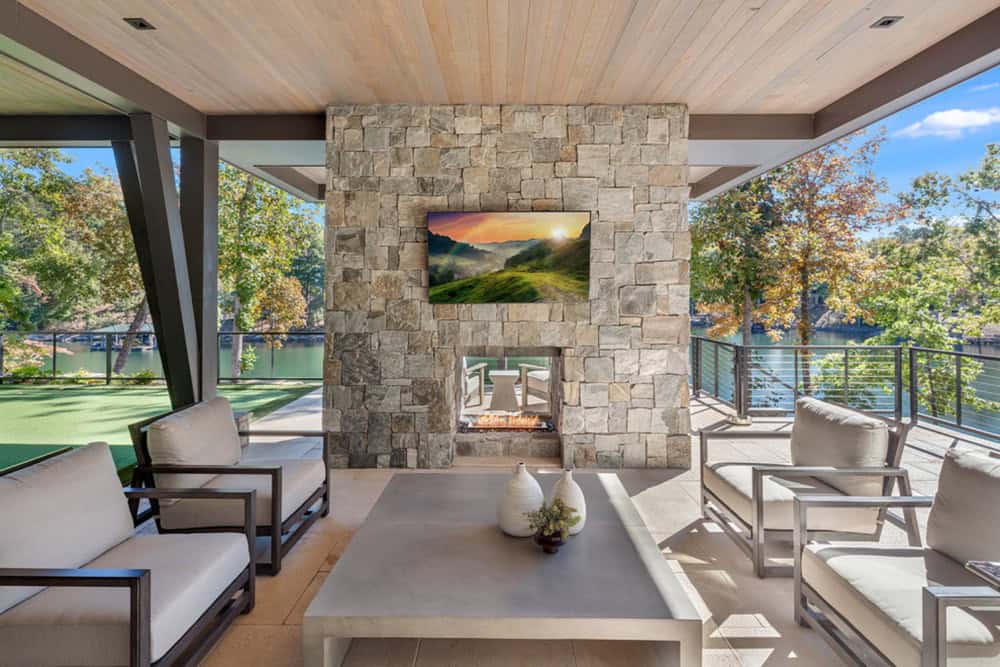 Outdoor fireplace with mounted TV flanked by patio seating and lake view