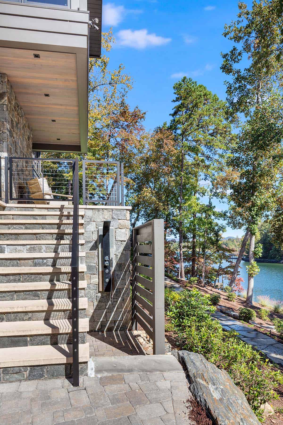 Exterior stairway and outdoor shower beside stone wall with lake view
