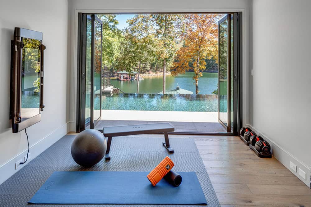 Home gym with yoga mat, dumbbells, and open doors framing a lake view