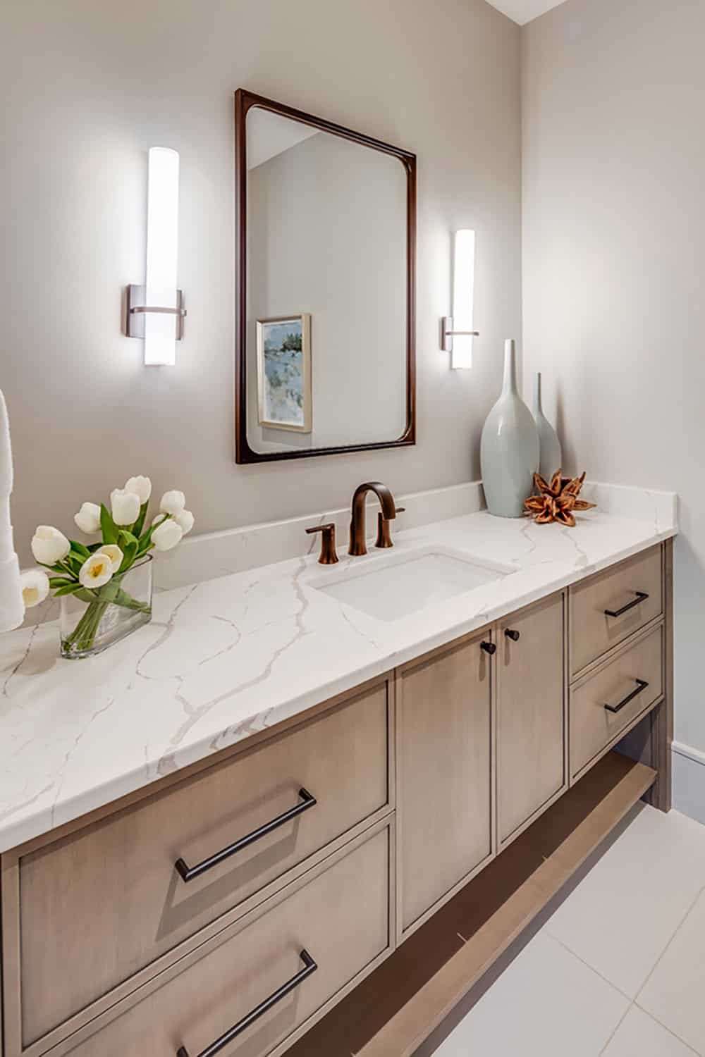 Bathroom vanity with marble countertop, bronze fixtures, and mirrored sconces