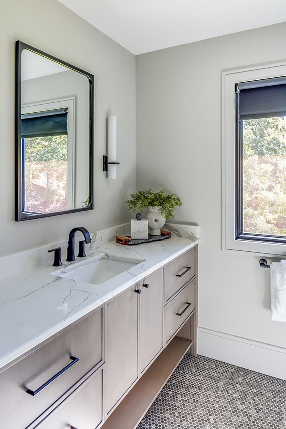 Bathroom vanity with black fixtures, mirror, and window with blackout shade