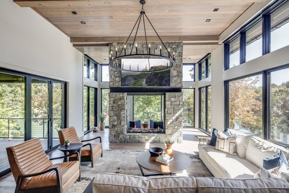 Great room with two-story stone fireplace, wraparound windows, and ring chandelier
