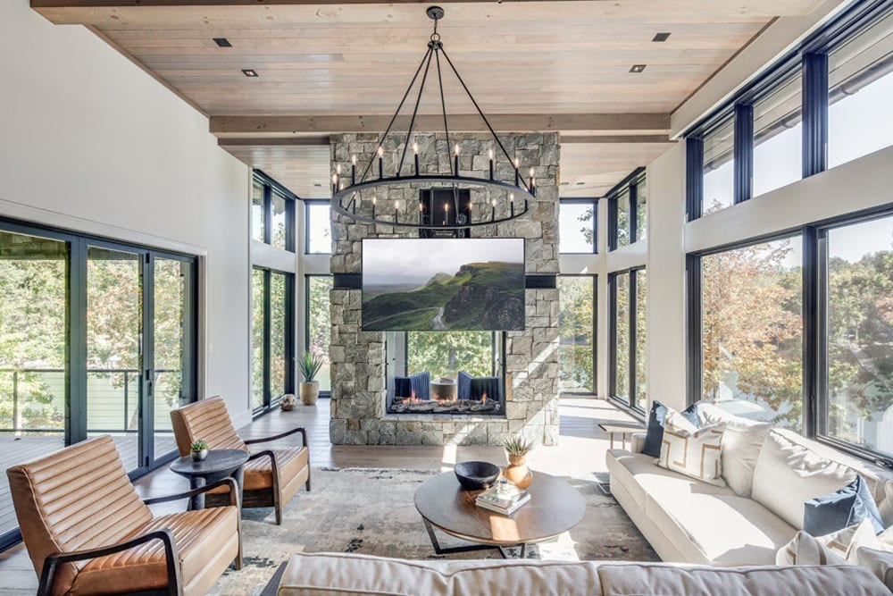 Living area with double-sided stone fireplace and mounted TV beneath a chandelier