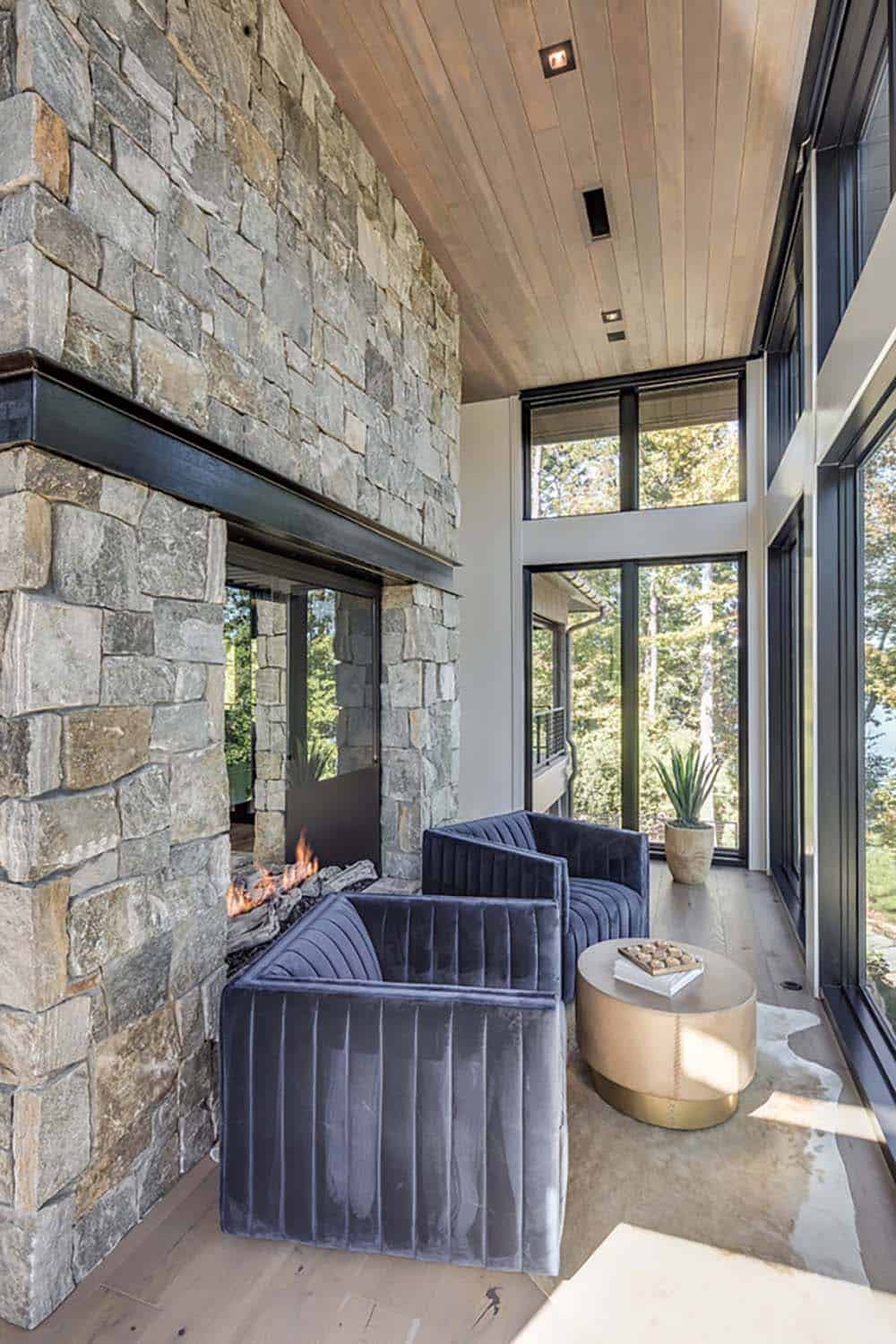 Sunroom nook with velvet armchairs beside a stone fireplace and brass side table