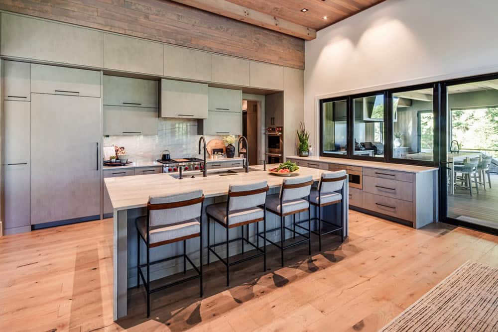 Kitchen island with bar seating and gray cabinetry opening to a covered deck