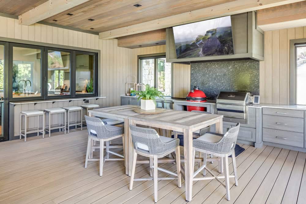 Covered outdoor kitchen and dining area with grill, TV, and bar seating
