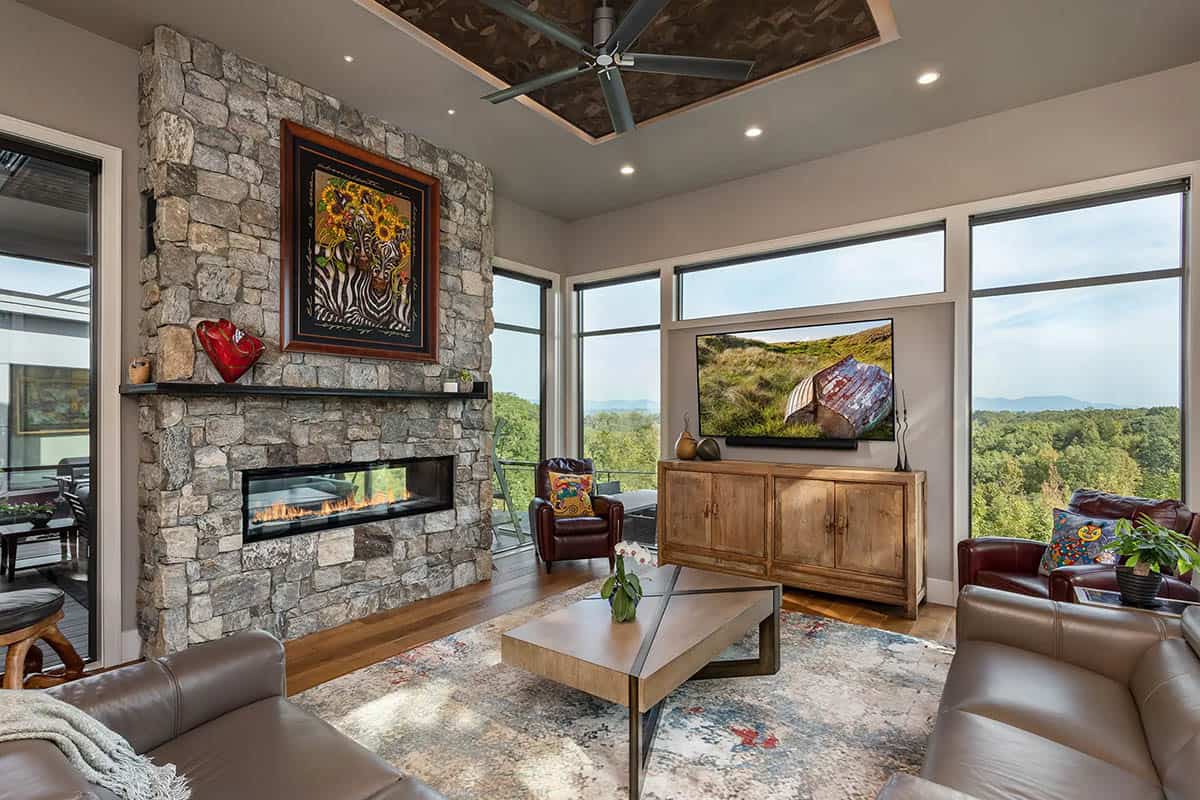Living room with stone fireplace, leather sofas, and mountain views