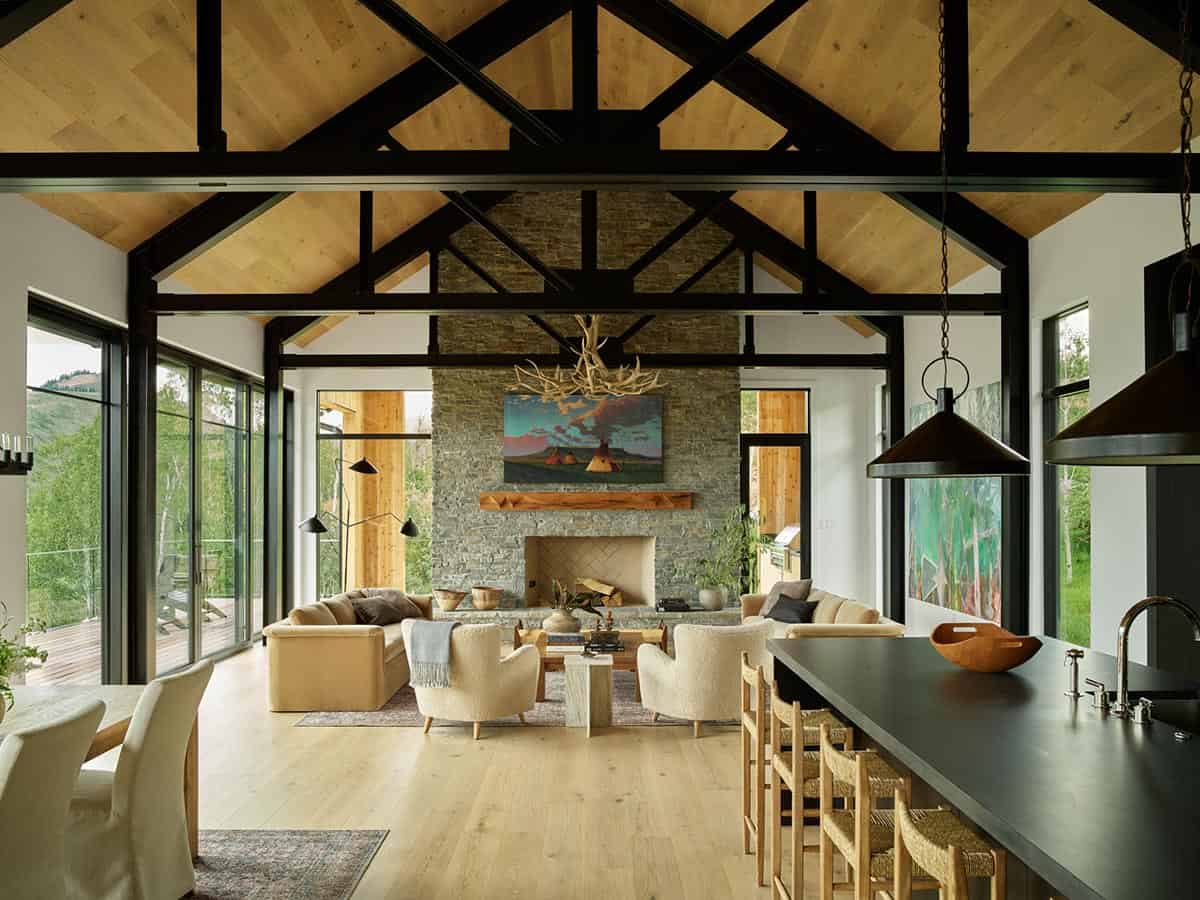 Vaulted great room with black steel trusses, stone fireplace, and mountain views