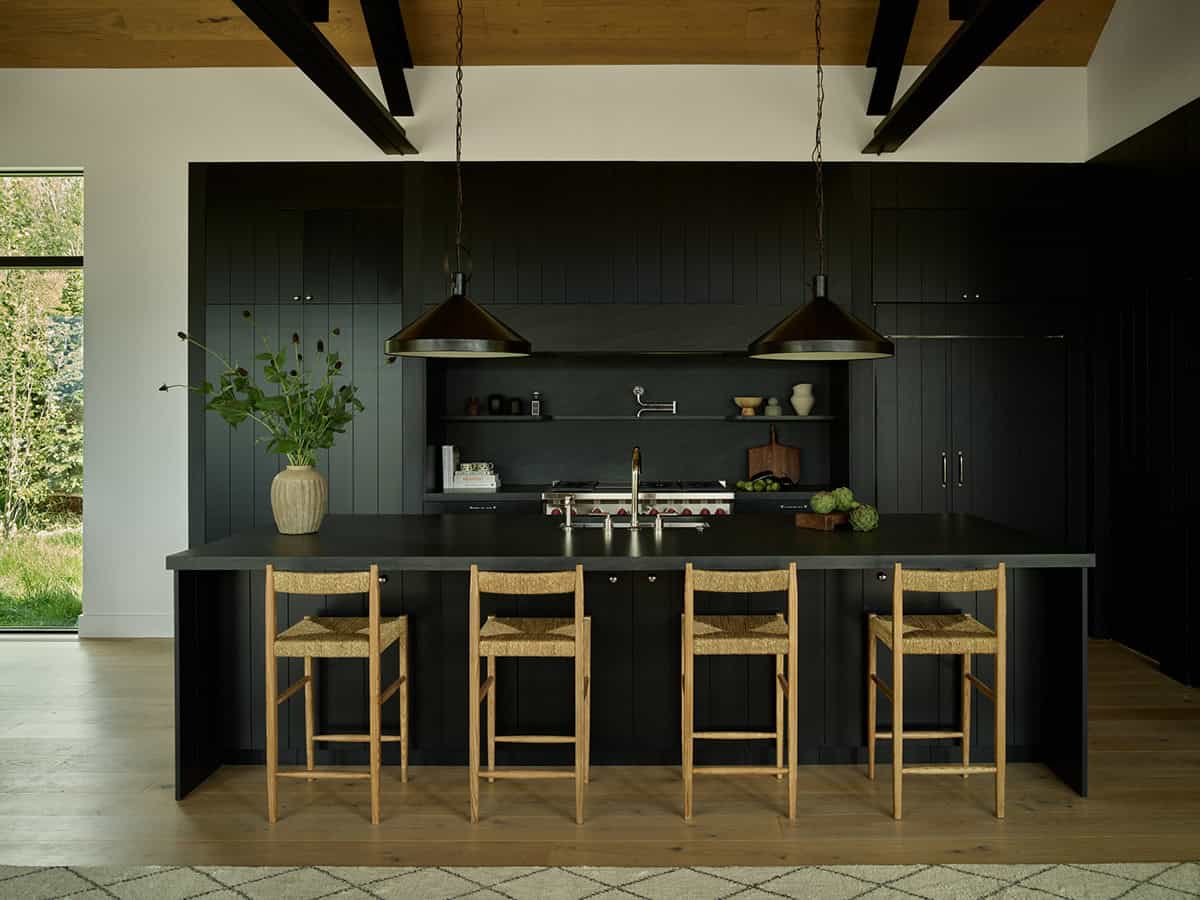 Black kitchen island with woven bar stools under wood beam ceiling